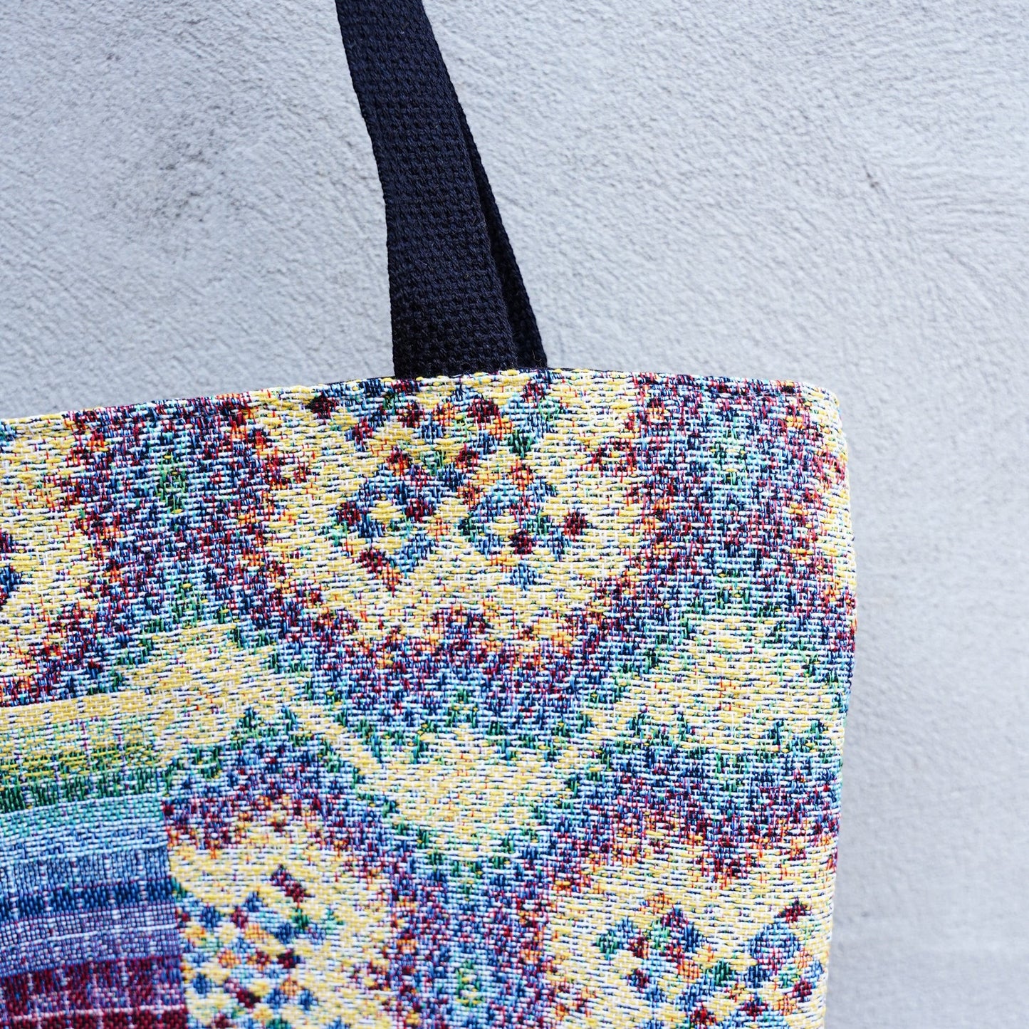 CoSM Shop Rainbow Cross woven tote bag with colorful tapestry exterior and black straps.
