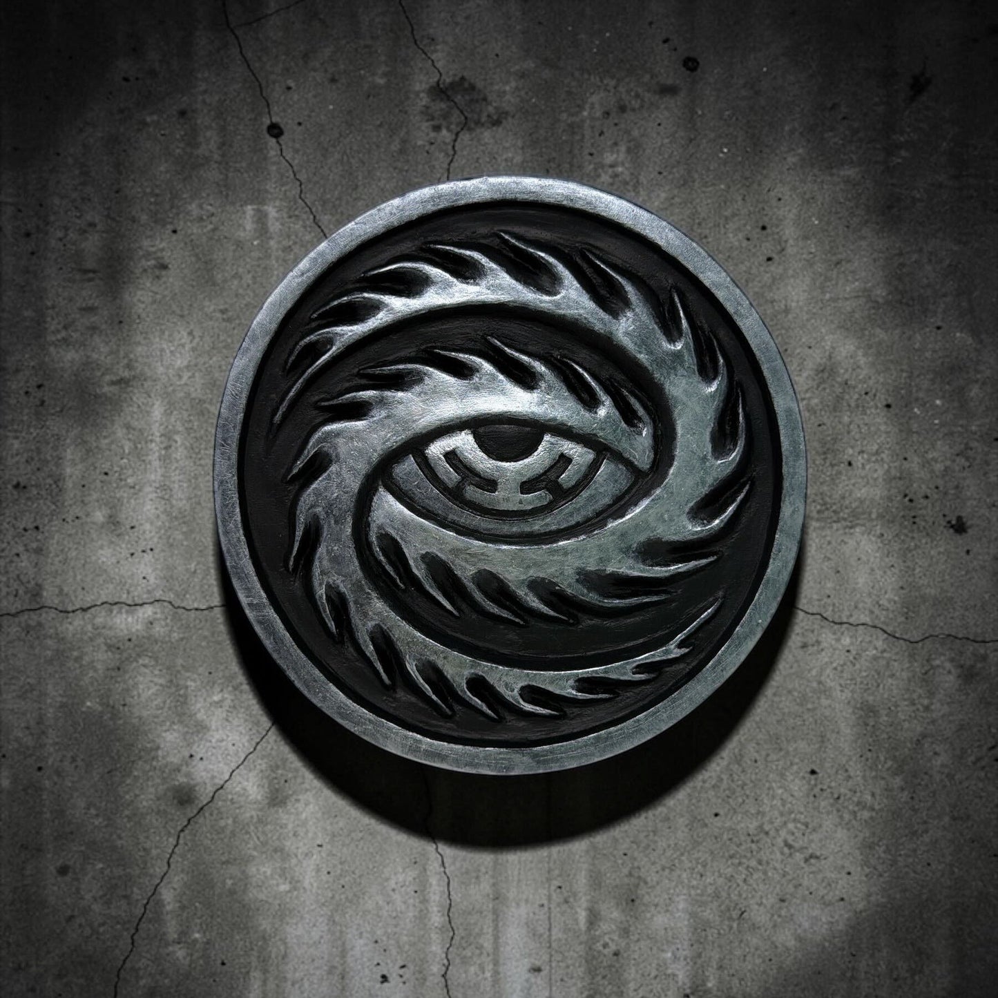 CoSM Shop Cosmic Eye wall emblem, a circular resin cast hand-painted with a stylized eye design in metallic silver and black.