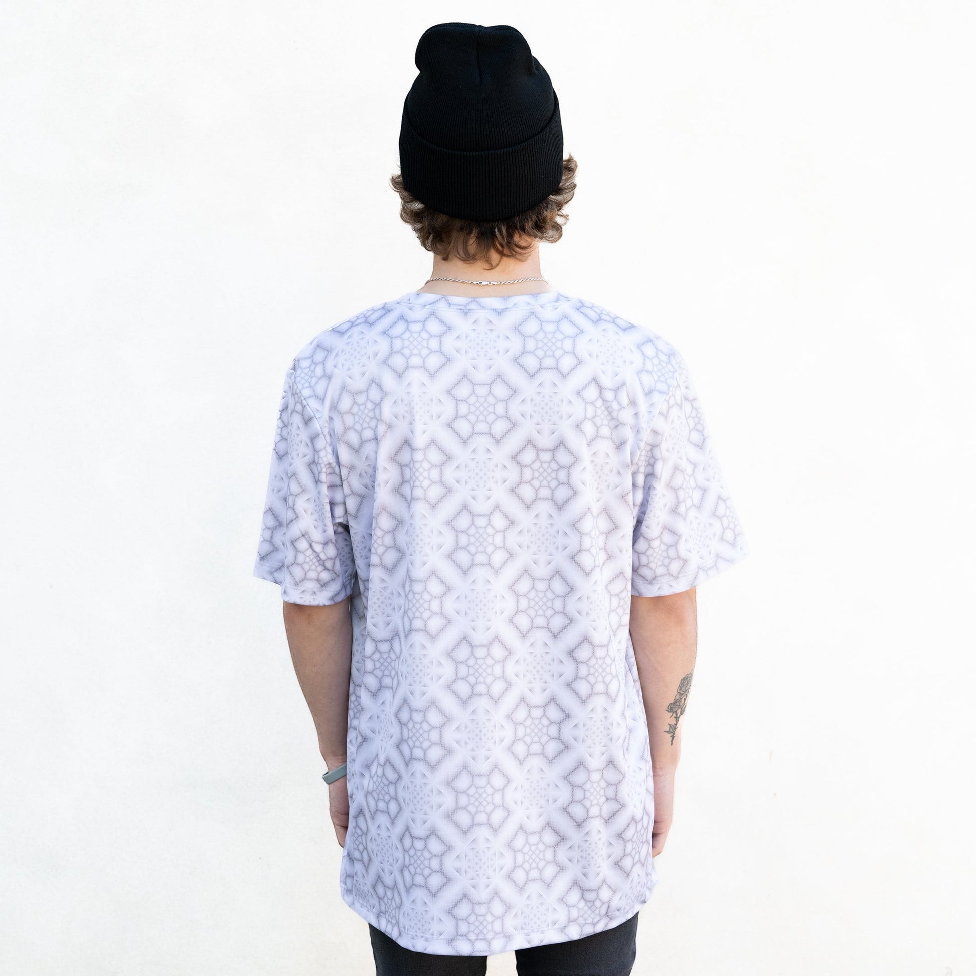 CoSM Shop white and grey all-over print dye-sub t-shirt with a geometric pattern, worn by a person with a black beanie.