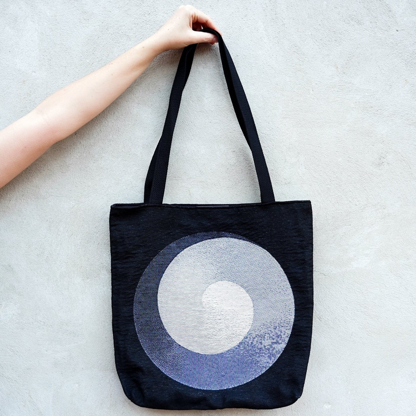 CoSM Shop Polar Unity Spiral woven tote bag with black handles and a grey and white spiral design on a black background.