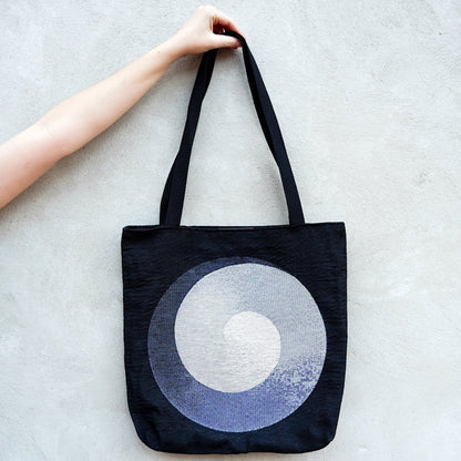 CoSM Shop Polar Unity Spiral woven tote bag with black handles and a grey and white spiral design on a black background.