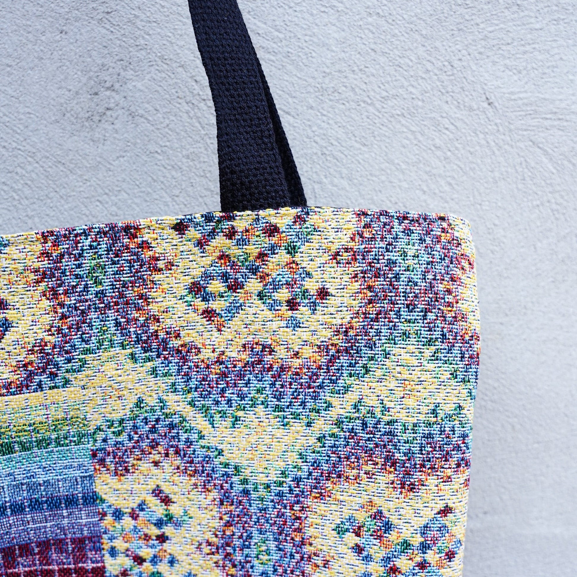 CoSM Shop Rainbow Cross woven tote bag with colorful tapestry exterior and black straps.