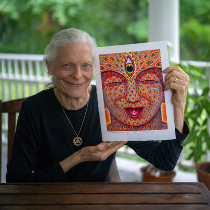 CoSM Shop Alex Grey holds a signed, limited edition paper print of his artwork "Third Eye Tears of Joy," featuring a colorful, multi-eyed face.