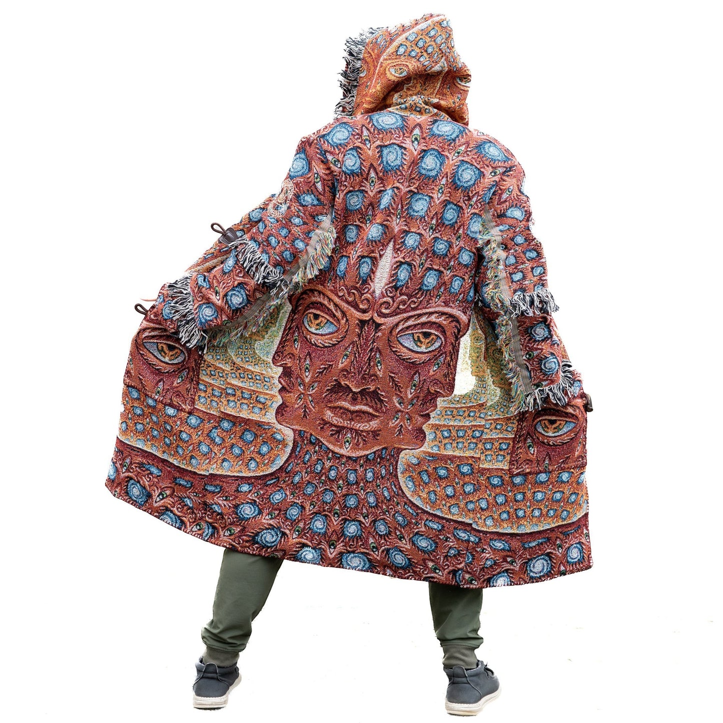 CoSM Shop unisex one-size woven coat with a hooded design and fringe trim, featuring a vibrant, intricate pattern of faces and eyes in earthy tones and blue.