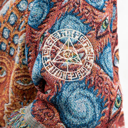 CoSM Shop unisex one-size woven coat with intricate eye and geometric patterns in blue, orange, and tan. Features embroidered emblem on sleeve.