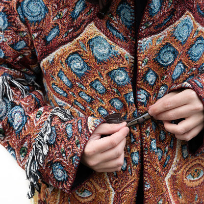 CoSM Shop unisex one-size woven cotton coat with a colorful geometric pattern and toggle closure. Features fringe detail on sleeves.