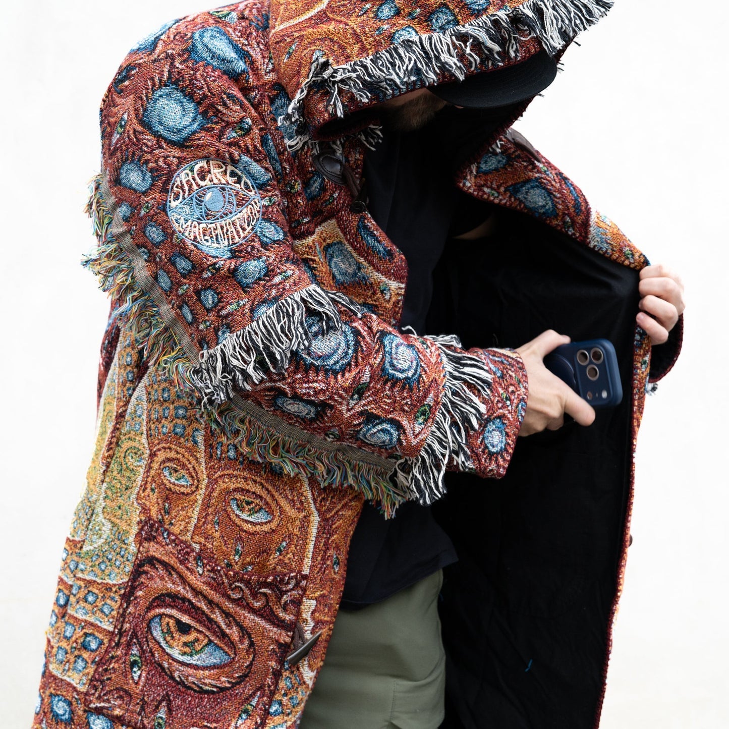 CoSM Shop unisex one-size woven cotton coat with fringe trim and a psychedelic eye pattern in red, blue, and yellow.
